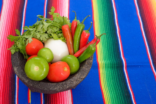 Molcajete met groenten op een kleurrijke serape Ingrediënten voor een hete saus