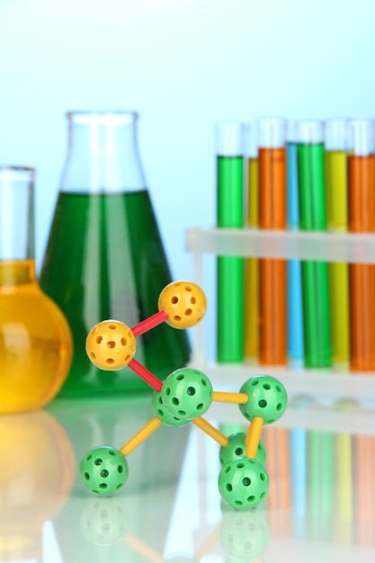 Molecuulmodel en reageerbuizen met kleurrijke vloeistoffen op blauwe achtergrond