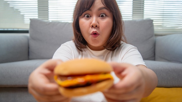 Mollige aziatische vrouw drukt geluk uit bij het eten van hamburger