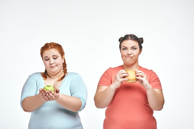 Mollige vrouwen de ene vrouw houdt een sandwich vast en de andere houdt een appel vast