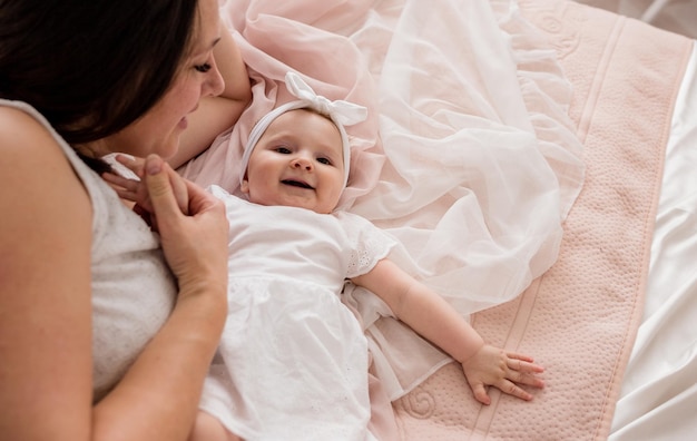 写真 ママと女の赤ちゃんが部屋のベッドに横たわって、部屋で遊んでいます