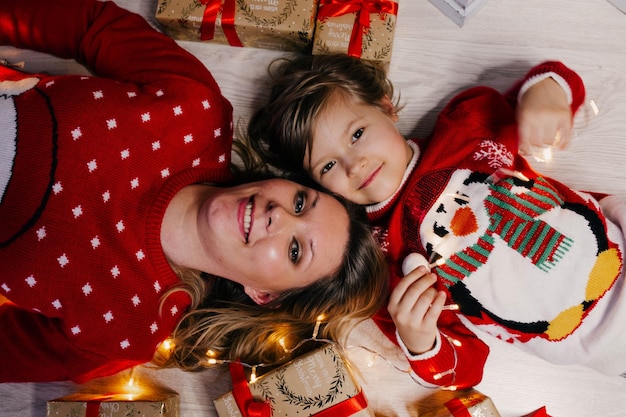 Фото Мама и дочь в рождественских свитерах сидят и лежат среди большого количества подарочных ящиков