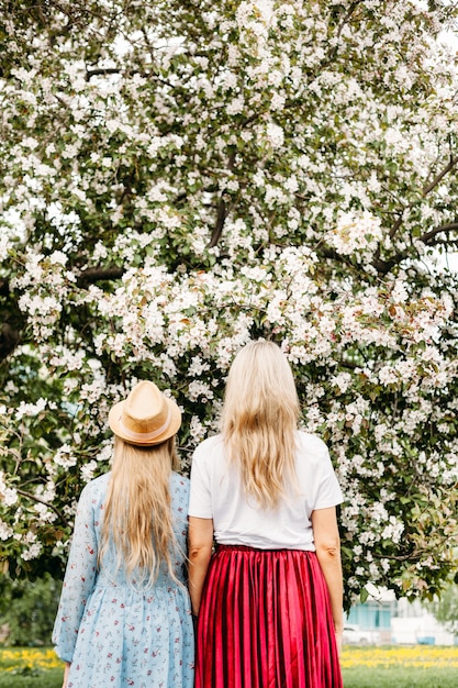 Фото Мама и дочь подростка снова возле цветущей яблони, прогулки по городу, вид сзади, яркая одежда