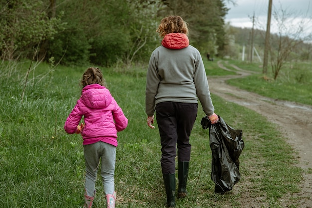 Мама и дочь мешками для мусора очищают окружающую среду от мусора.