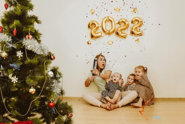 Фото Мама и дочери с настоящими эмоциями радости взрывают конфетти в новом году 2022