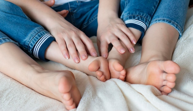 Photo mom and baby are sitting in blue jeans on the bed with bare feet