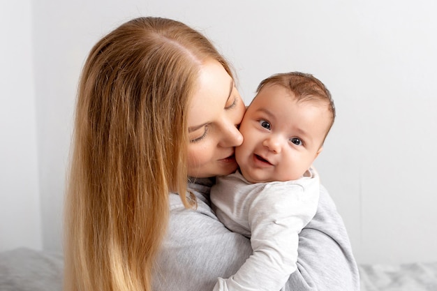 Mamma e bambino giocano sul letto madre e figlio famiglia felice bella ragazza bionda e bambino carino a casa