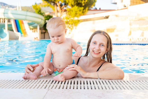 Mom and baby in the pool with water slides in the summer have fun swimming, relaxing and spending time with the family on vacation