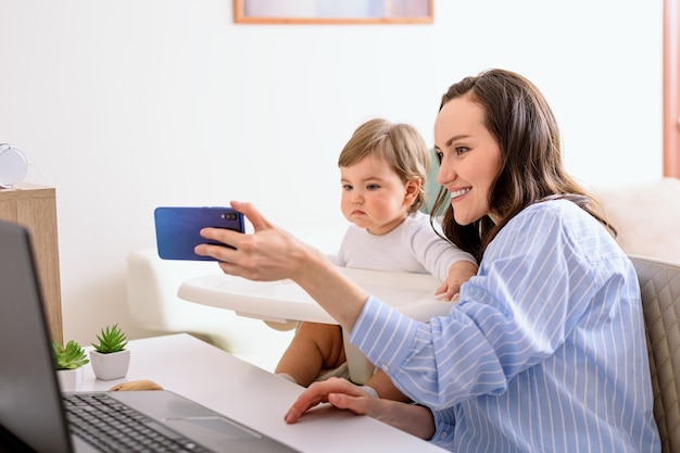 Mamma in camicia blu e figlia parlano tramite video, videochiamate, selfie, maternità