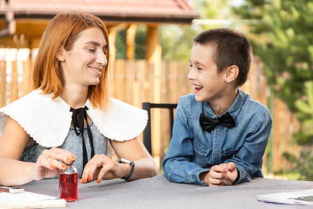 Mom and boy schoolboy are engaged in lessons through a laptop at home in the garden. Online classes for children. Schoolboy listens to a lecture and solves problems