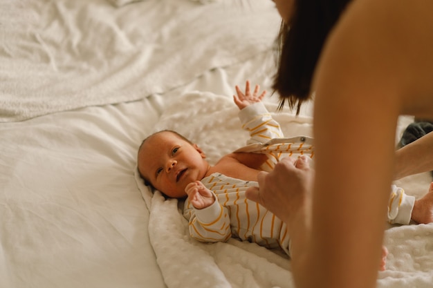 Mom changing his diaper newborn baby. Happy young mother playing with baby while changing his diaper on bed.