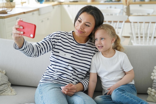 ママと子供がスマートフォンで自分撮りをしている家族は家で抱きしめたり笑顔で楽しんでいます