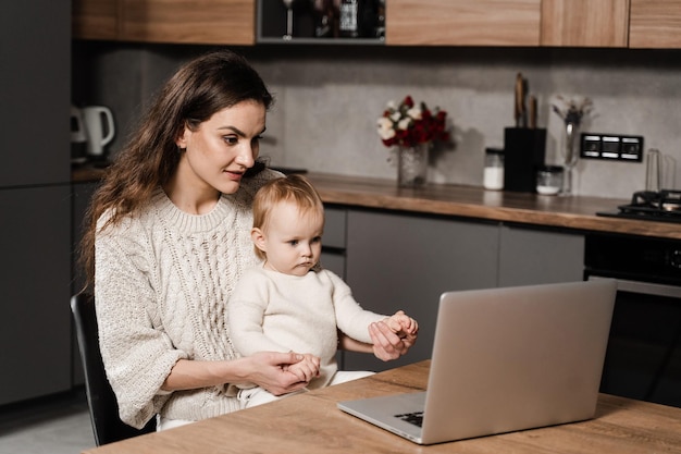 Mom and child daughter communicate with dad via video communication on laptop Maternity and childhood Toddler child watches cartoons with her mother in the kitchen