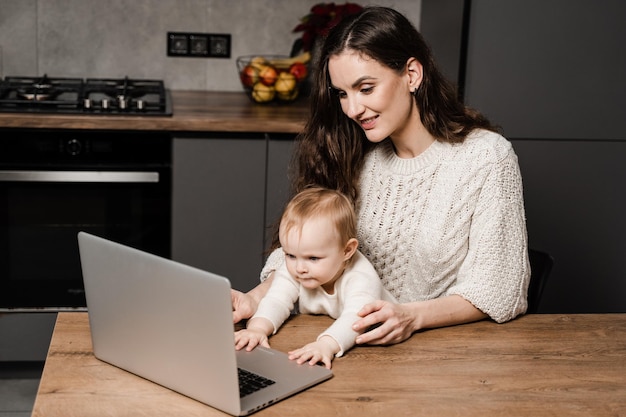 Mom and child daughter communicate with dad via video communication on laptop Maternity and childhood Toddler child watches cartoons with her mother in the kitchen