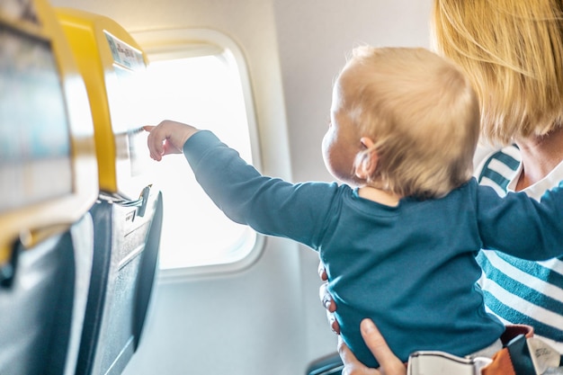 Mom and child flying by plane mother holding and playing with her infant baby boy child in her lap d