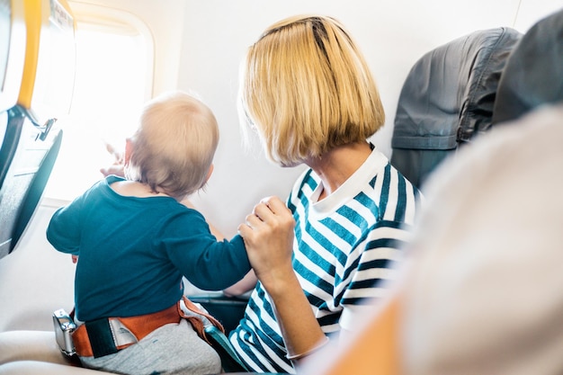 Mom and child flying by plane Mother holding and playing with her infant baby boy child in her lap during economy comercial flight Concept photo of air travel with baby Real people