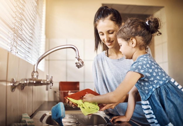 Mom child and washing dishes in kitchen with cleaning teaching and help in a family home Learning happy and love of parent and young girl together with bonding support and sink with care
