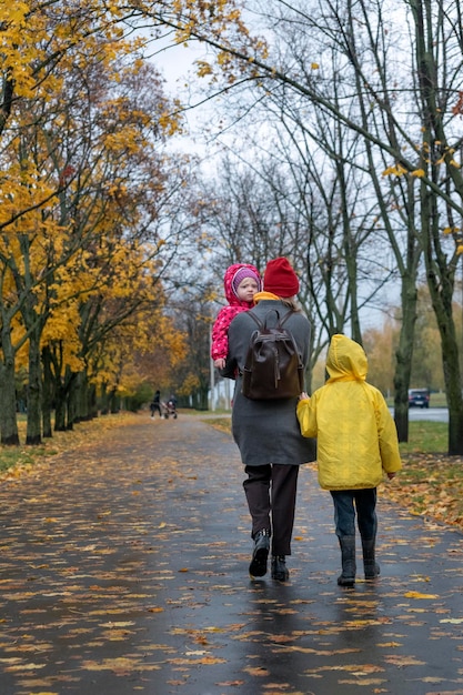 엄마와 아이들이 비오는 가을 공원에서 걷고 있습니다. 세로 프레임