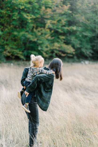 Foto mamma corregge una bambina sulla schiena mentre è in piedi sul prato lato vista