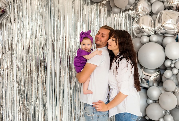 Mom, dad and baby hugging on a festive background with gray balloons