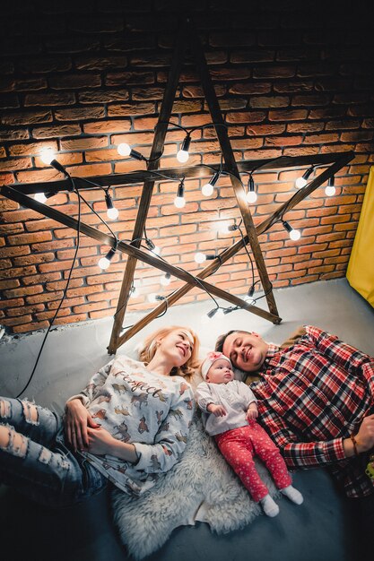 Mom, dad and baby lie on a woolen carpet and smile