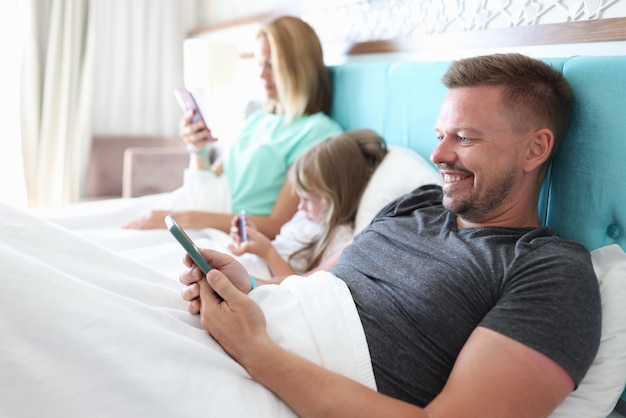 Mom, dad and daughter lie in bed and look at phone.