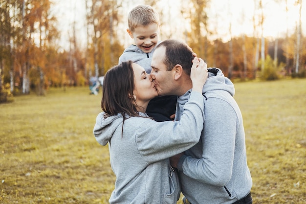 Mom and dad holding their son on their shoulders while they kiss and the child happily watches spend...