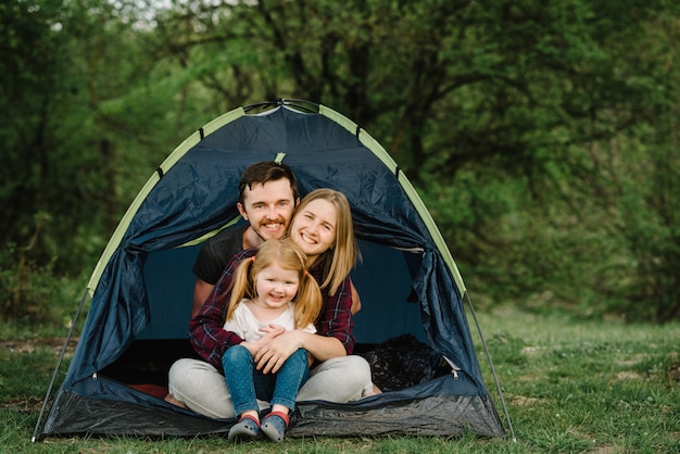 Mom, dad hugs a kid and enjoying a camping holiday in the countryside