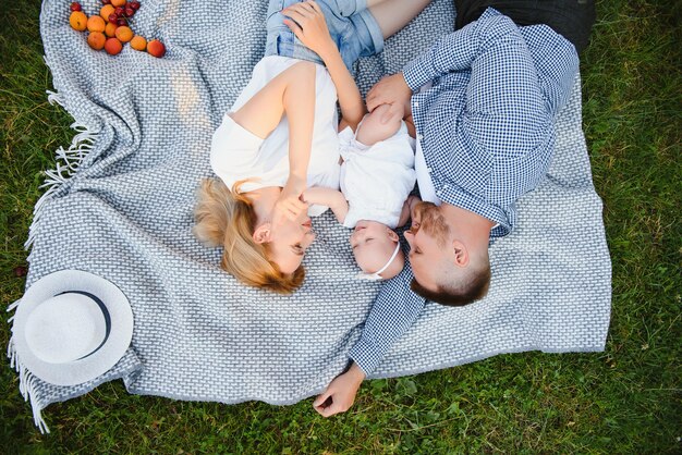 Mom, dad and little son lying on the blanket in the summer park. The concept of summer holiday. Mother's, father's, baby's day. Family spending time together on nature. Family look