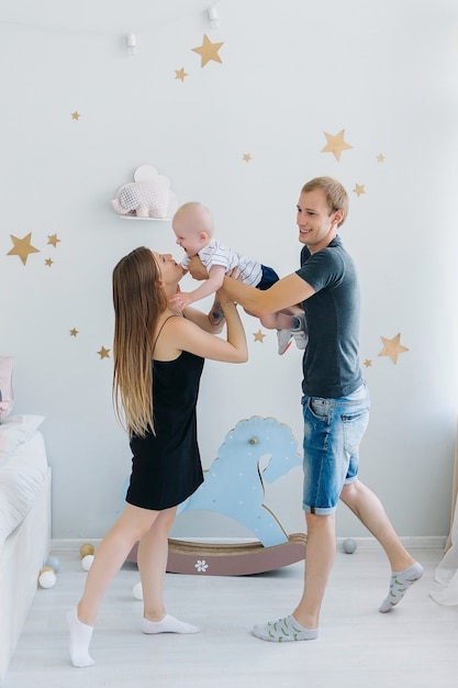 Photo mom and dad plays with her son, holding him in they arms. home children cozy interior.