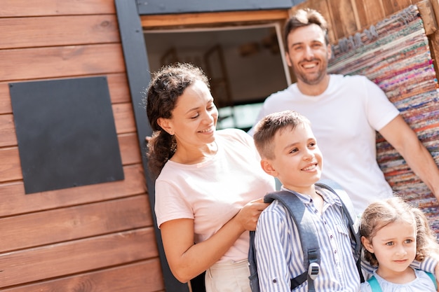 Mamma e papà portano i loro due figli a scuola, è il primo giorno di scuola dopo le vacanze estive, la mamma controlla se lo zaino della scuola di suo figlio è pesante.