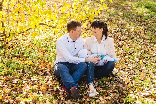 Mamma e papà con un bambino, un ragazzino che cammina in autunno nel parco o nella foresta. foglie gialle, la bellezza della natura. comunicazione tra un bambino e un genitore.