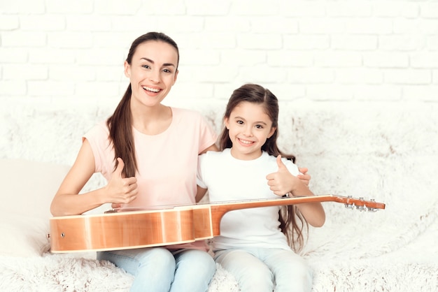 Photo mom and daughter are have a guitar on their laps.