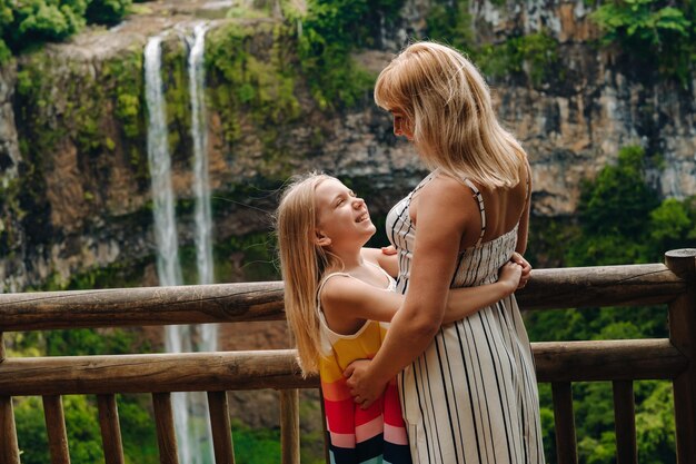 Mom and daughter are hugging each other near a waterfall in Chamarel Park on the island of Mauritius