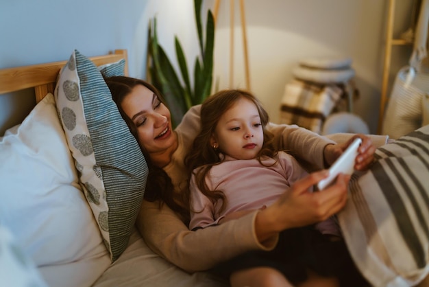 Mom and daughter are lying in bed and are considering something in a tablet pc