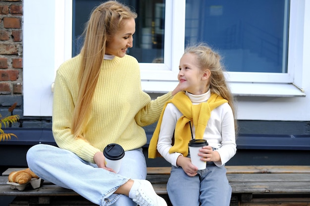 Mom and daughter are sitting on a bench with glasses of hot chocolate and croissants the family spen