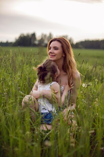 Photo mom and daughter are sitting in a green field in white t-shirt