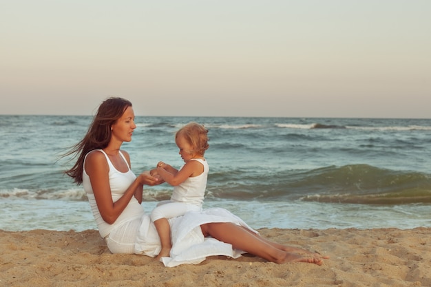 Mamma e figlia sono sedute sulla sabbia sulla spiaggia vicino al mare