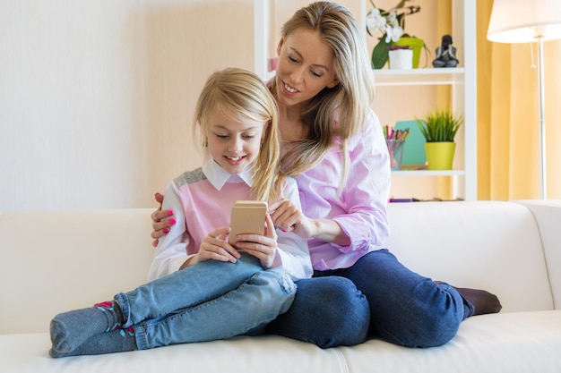 Mom and daughter are using phone while sitting on the couch