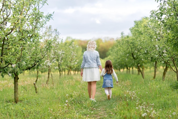 Mom and daughter are walking through the spring garden Photo from the back