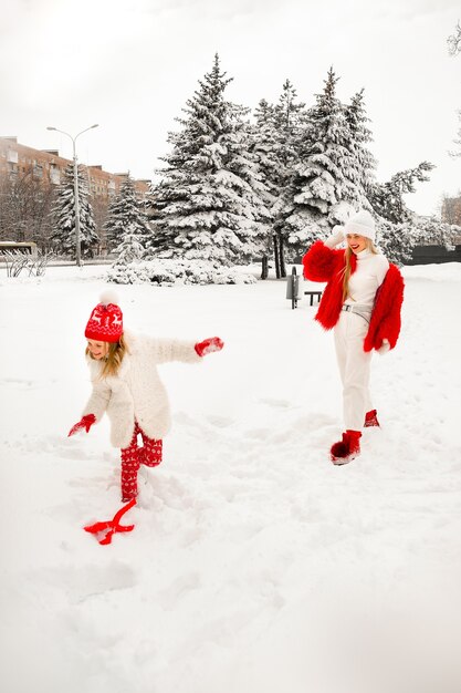 美しい冬服を着たママと娘がウィンターパークで雪玉を遊んでいます。ファミリールック