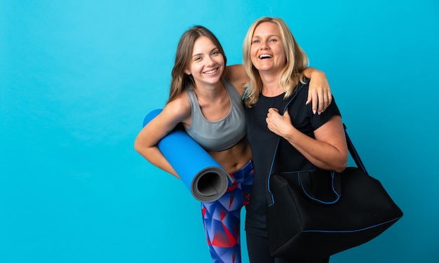 Mom and daughter doing yoga isolated on blue wall