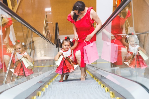 Mom and daughter in dresses in the mall with l bags