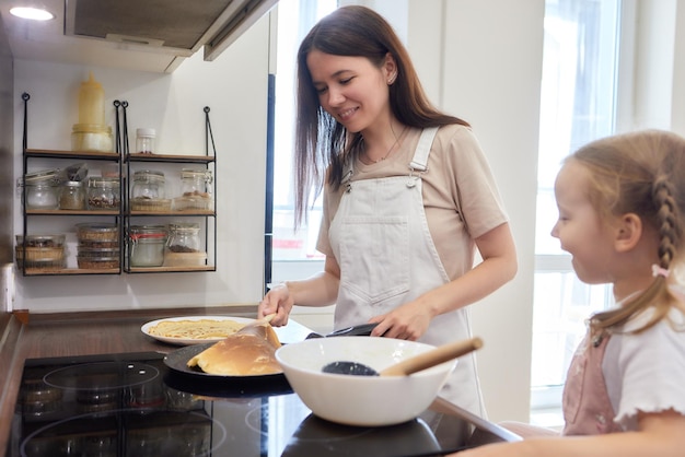 Mom and daughter fried pancakes together in the kitchen in a bright interior moms assistant and brea