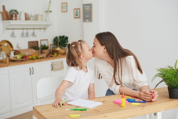 ママと娘は宿題を終えて、幸せでキスをします。子供の世話をし、宿題を手伝うという概念。