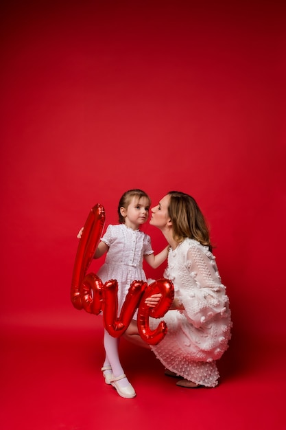 Mom and daughter hug and hold an air foil balloon love on red