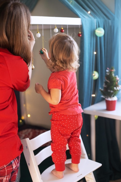 写真 クリスマスの子供部屋を飾る赤いパジャマのママの娘