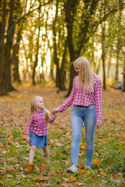Мама и дочь в джинсах и розовых рубашках гуляют в осеннем парке.