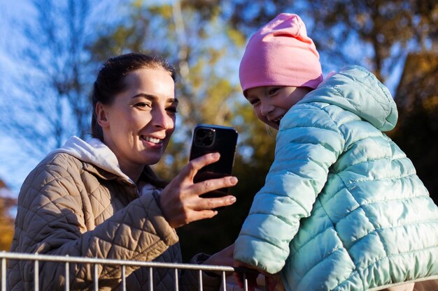 Mom and daughter joyfully look at something on the phone in the park