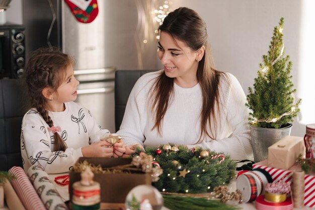 Mom and daughter making christmas wreath using fresh pine branches and festive decorations christmas